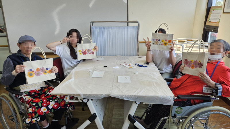 어르신과 학생들이 함께 만든 압화에코백을 들고 있는 모습