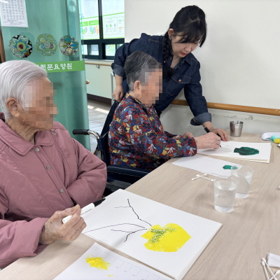 여자 어르신 2명이 그림 그리고 있고, 여자 선생님이 도와주고 있는 모습