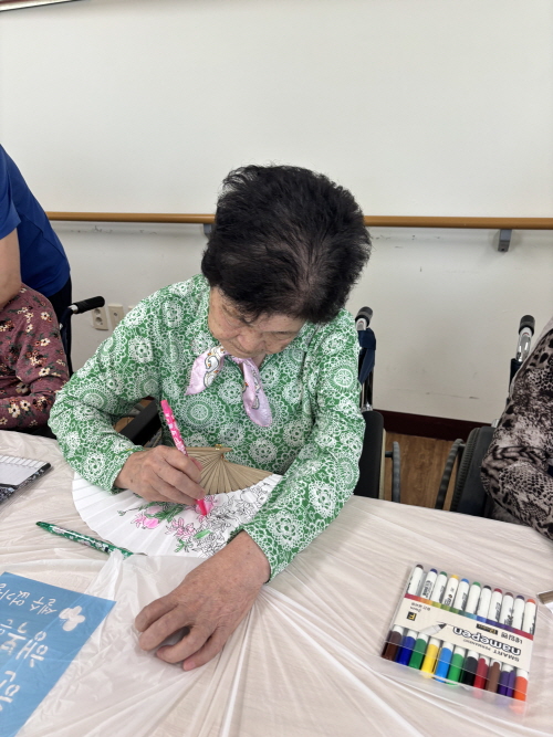 여자 어르신이 부채에 그림 그리고 있는 모습