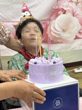 꼬깔모자를 쓴 여자 어르신이 생일케이크 촛불 부는 모습