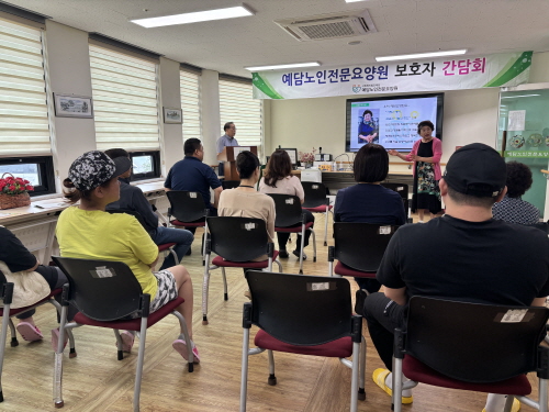 정면에 현수막과 TV 화면이 보이고 10여명이 앉아 있으며 여자분이 화면을 가르키며 설명하고 있다