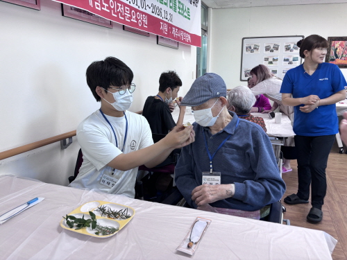 남학생이 남자 어르신 코에 무언가를 갖다대며 냄새를 맡게 하고 있다