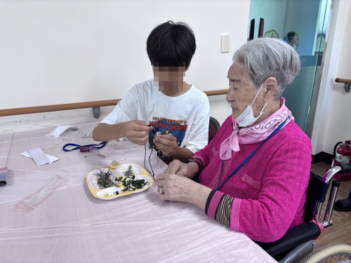 남자 학생과 여자 어르신이 같이 무언가를 만들고 있다