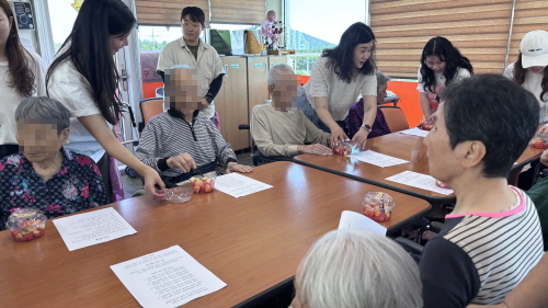테이블에 앉아 계신 어르신들에게 청년들이 과일을 드리는 모습