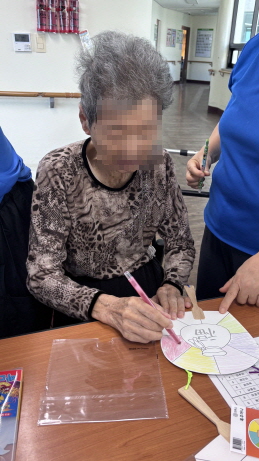 여자 어르신이 부채에 색칠하고 있다